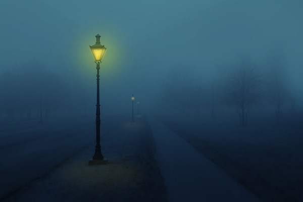 un réverbère éclairé au gaz brille faiblement dans la nuit et le brouillard