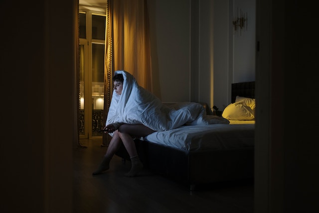 une jeune femme emmitouflée dans sa couette et assise sur son lit regarde la télé sans pouvoir dormir