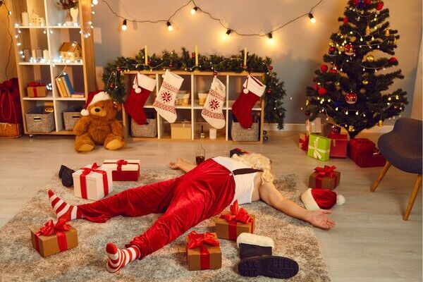 un père noel épuisé est endormi devant la cheminée d'un appartement au milieu des cadeaux.